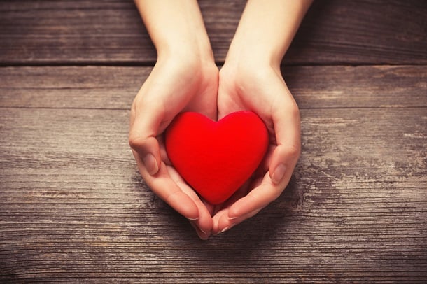 Hands holding a heart made out of red material.